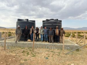 Men standing in front of two large water tanks in Culli Alto, Bolivia