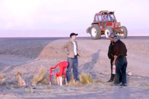 3 men engaged in conversation standing outside in Culli Culli Alto, with a bulldozer in the background